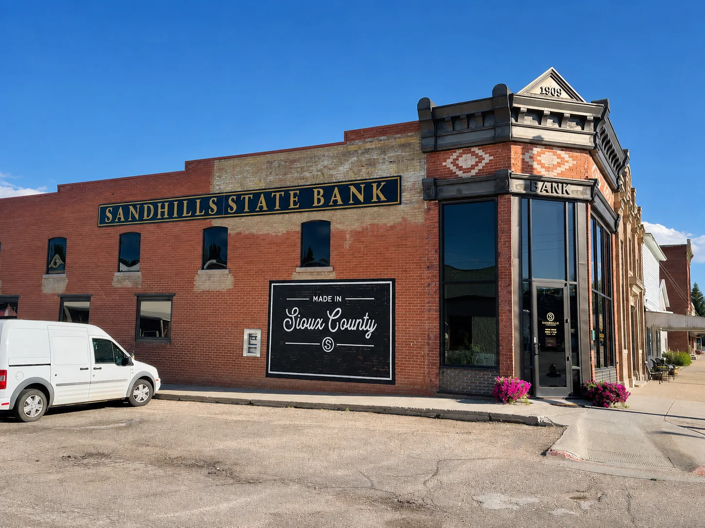 Historic brick Sandhills State Bank branch in Harrison, Nebraska, with a black-and-white Made in Sioux County wall mural