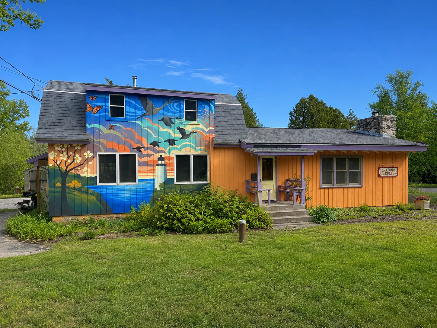 Wide exterior view of Backroads Deli with The Long Return mural across the building
