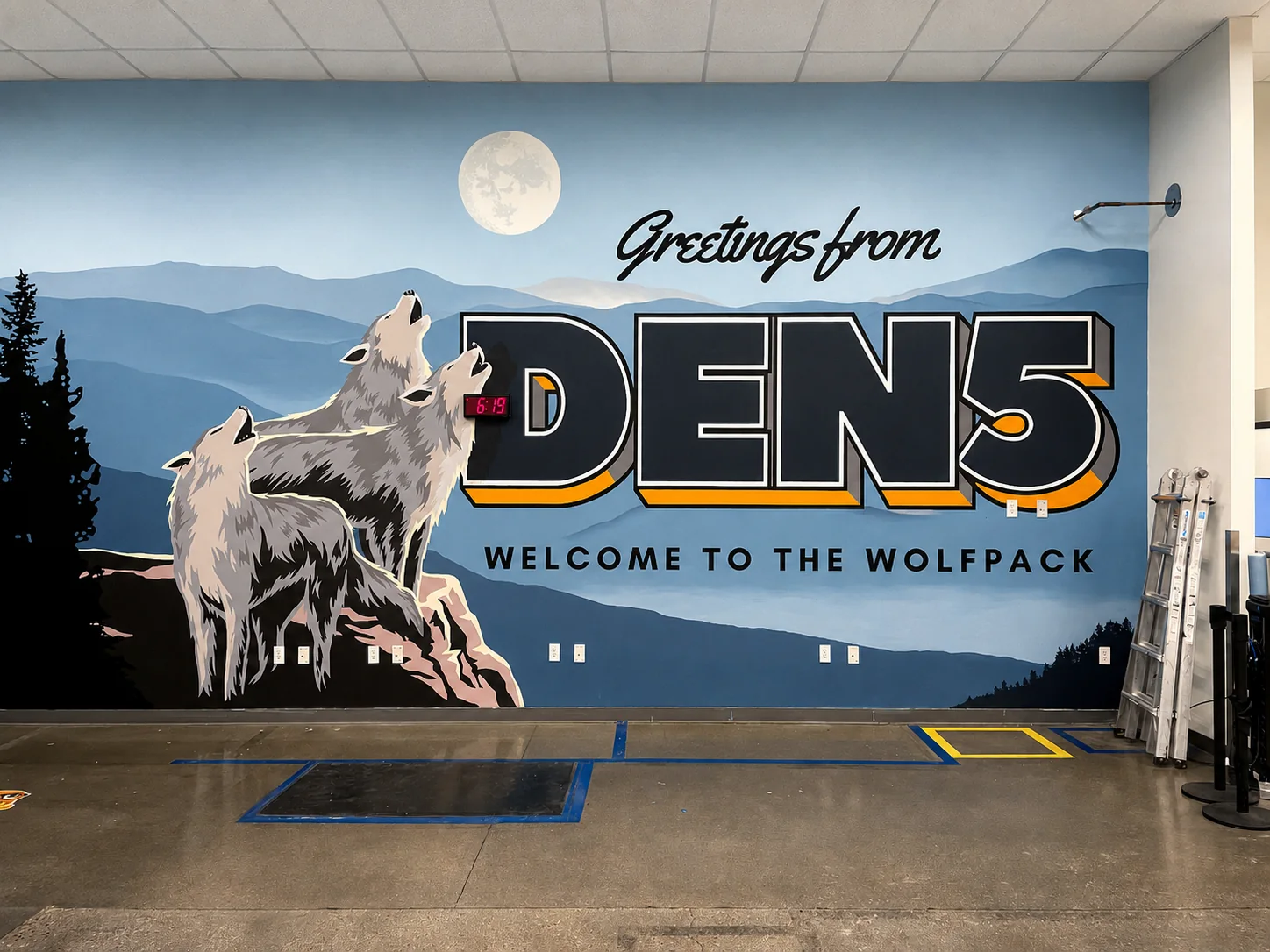 Large Welcome to the Wolfpack mural with wolves, layered mountains, pine trees, a moon, and bold DEN5 lettering