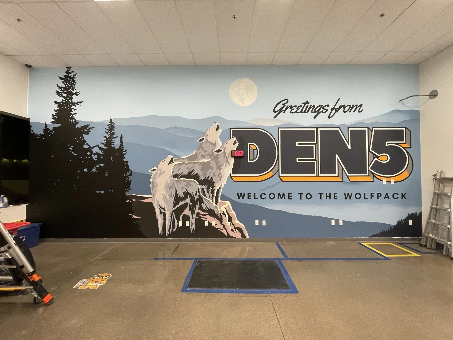 Large branded mural with three wolves, layered mountains, pine trees, and bold Wolfpack lettering